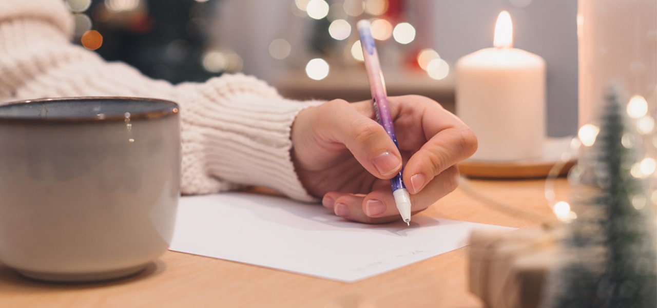 Woman's hand writing a list with a mug, candle and holiday decorations next to her