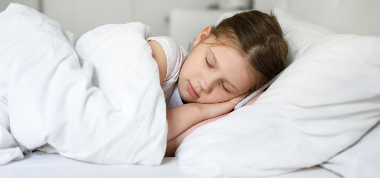 School-aged girl sleeping on her bed, resting her head on her hands 