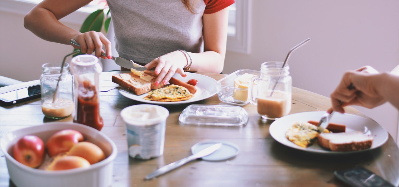 Cropped image of two people sitting at the breakfast table, showing hands preparing food