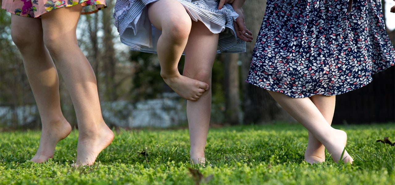 Cropped photo of three small children in bare feet omn the grass, shown from the knees down