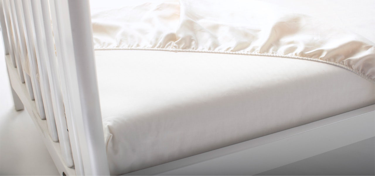 Fitted orgqnic crib sheet pulled up to reveal organic crib mattress 