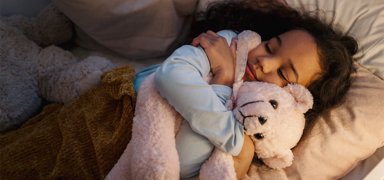 Young girl, snuggling a teddy bear, sound asleep in bed