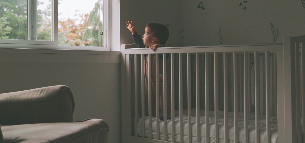 Toddler standing in crib and looking out a nearby window