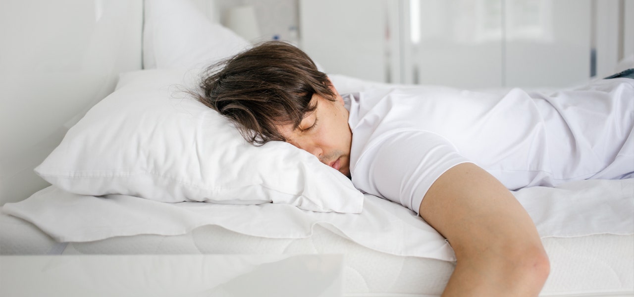 Man sleeping on his stomach, arm hanging off the bed