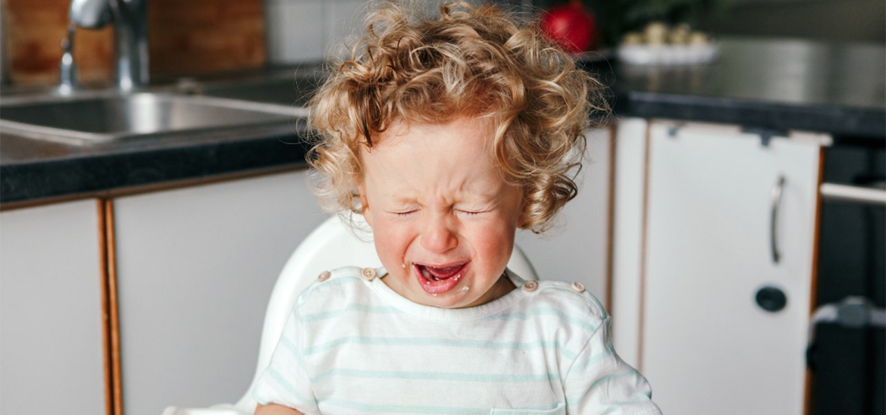 Fussy baby eating rice cereal in their high chair