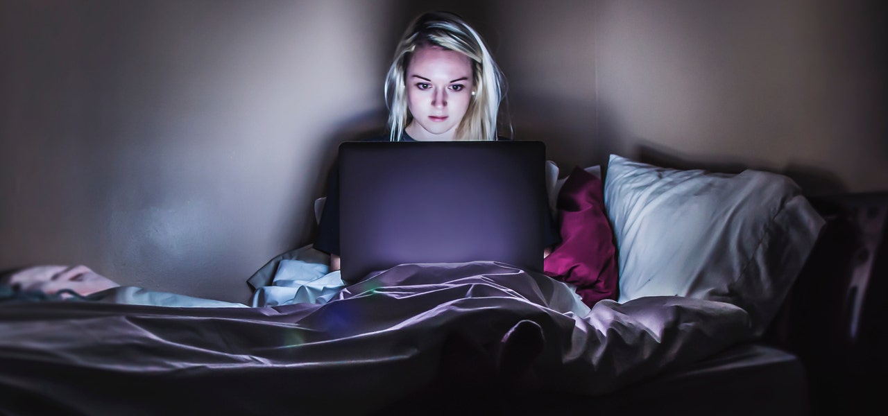 Woman sitting up in bed in a dark room in the blue light glow of her laptop