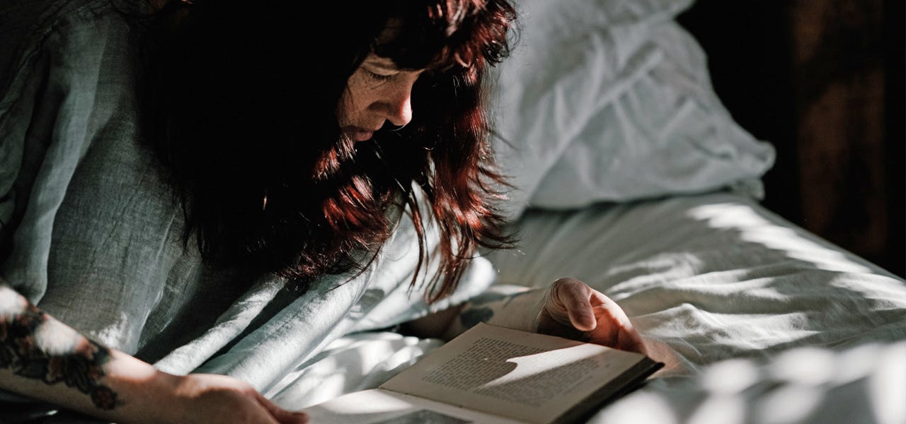 Woman lounging in bed and reading a book