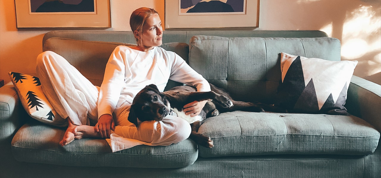 Woman in her pajamas, snuggling her dog on the couch 