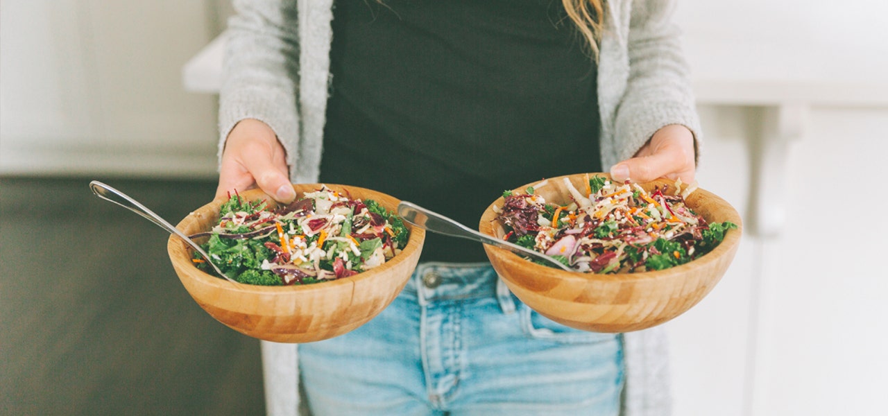 Woman's hands holding wooden bowls of salad