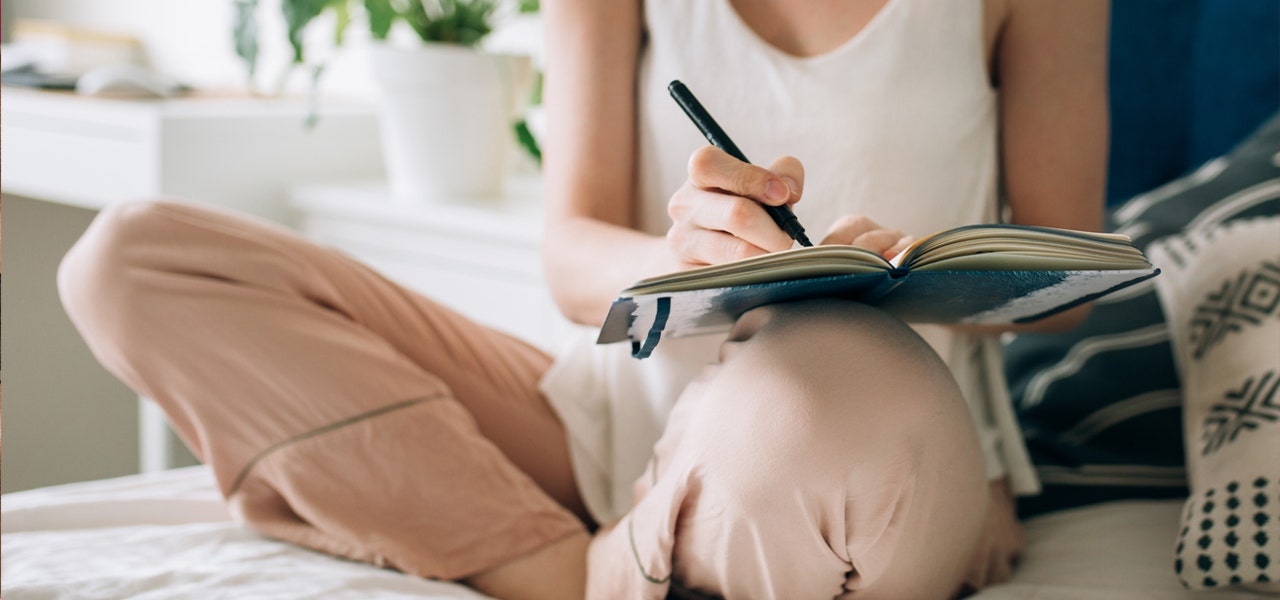 Woman sitting cross-legged on bed and writing in a journal