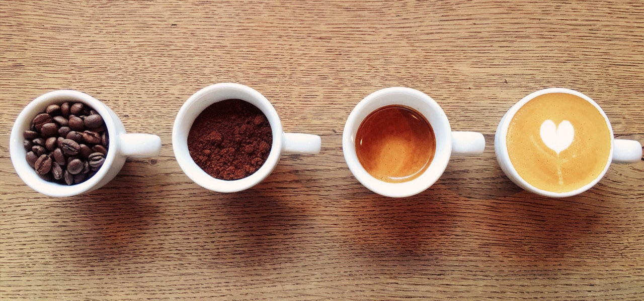 Overhead image of four mugs showing coffee beans, ground espresso, espresso and cappuccino 