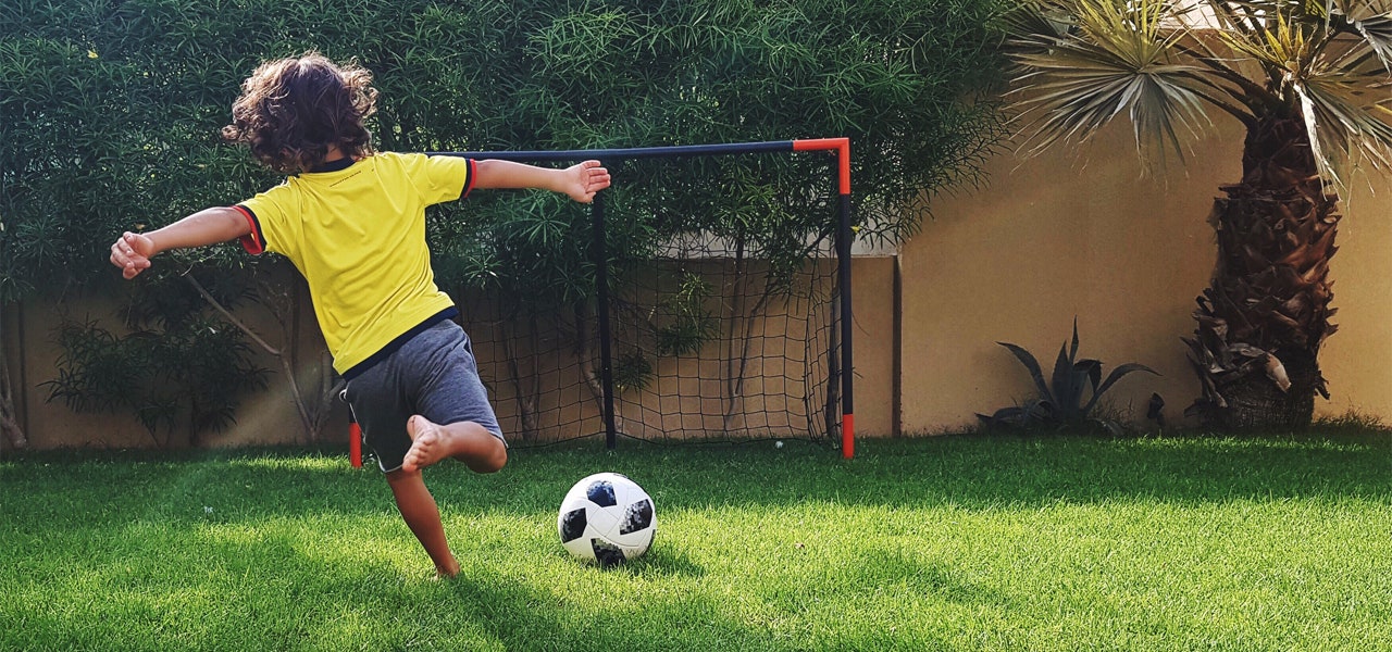 School-aged child kicking a soccer ball in the backyard