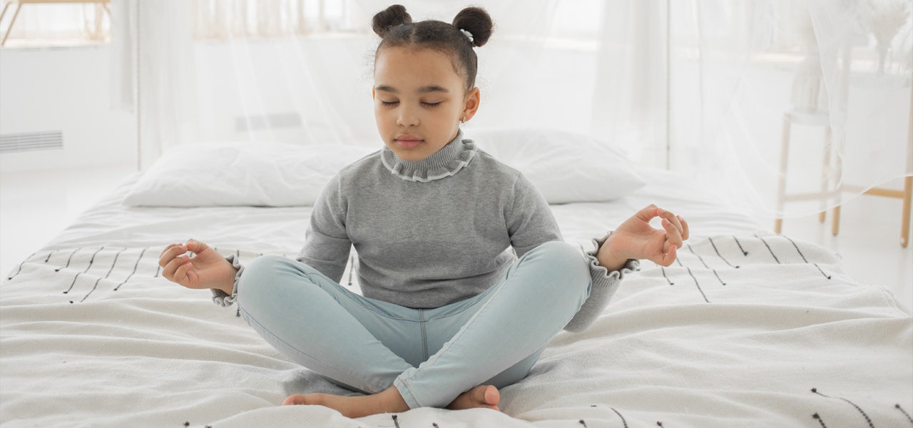 Elementary-aged girl meditating on her bed