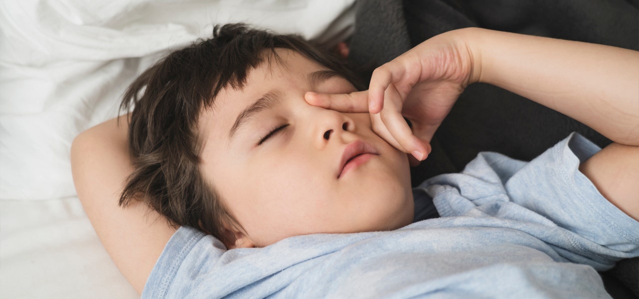 Young boy sleeping on his back and rubbing his eyes