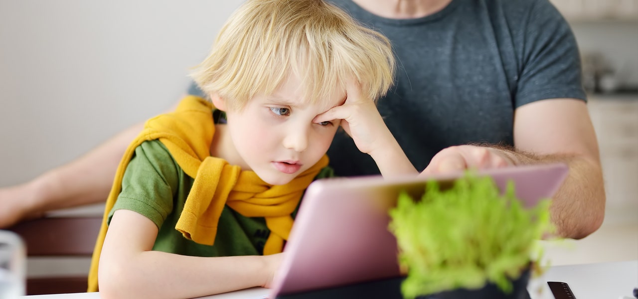 Small child looking exhausted while trying to do homework on a laptop