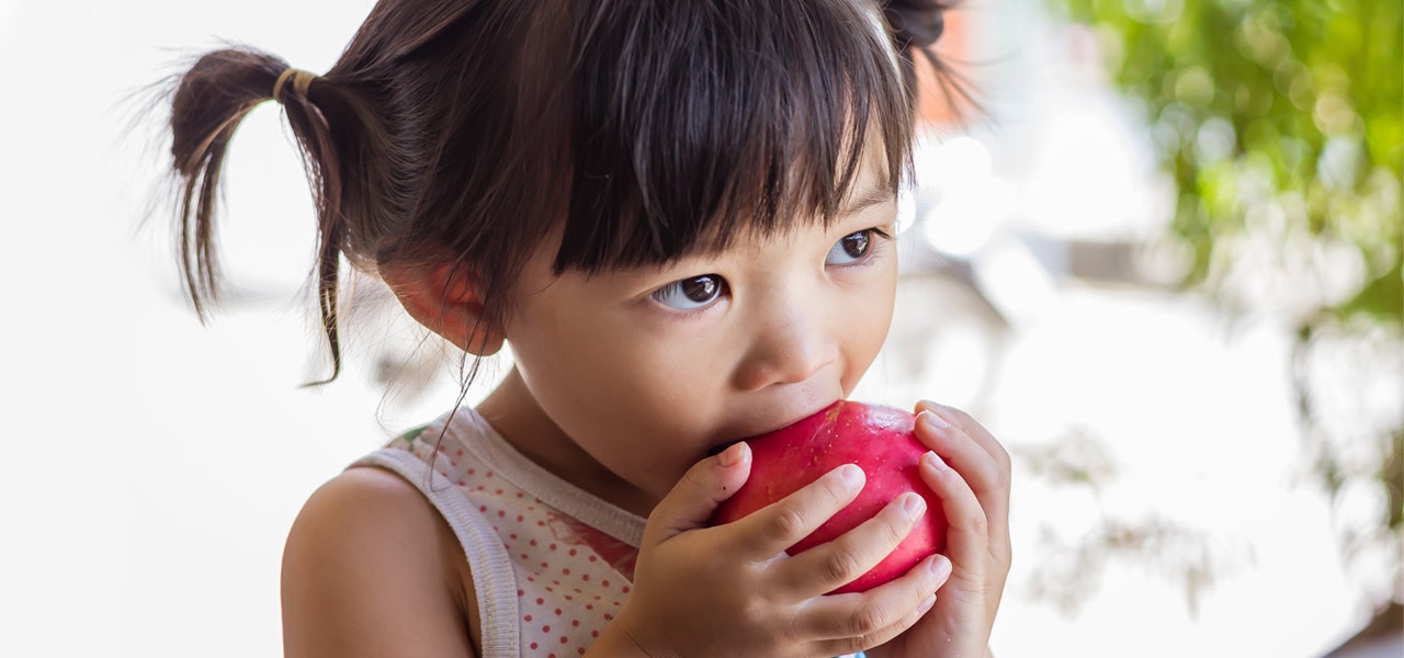 Little girl biting into a red apple