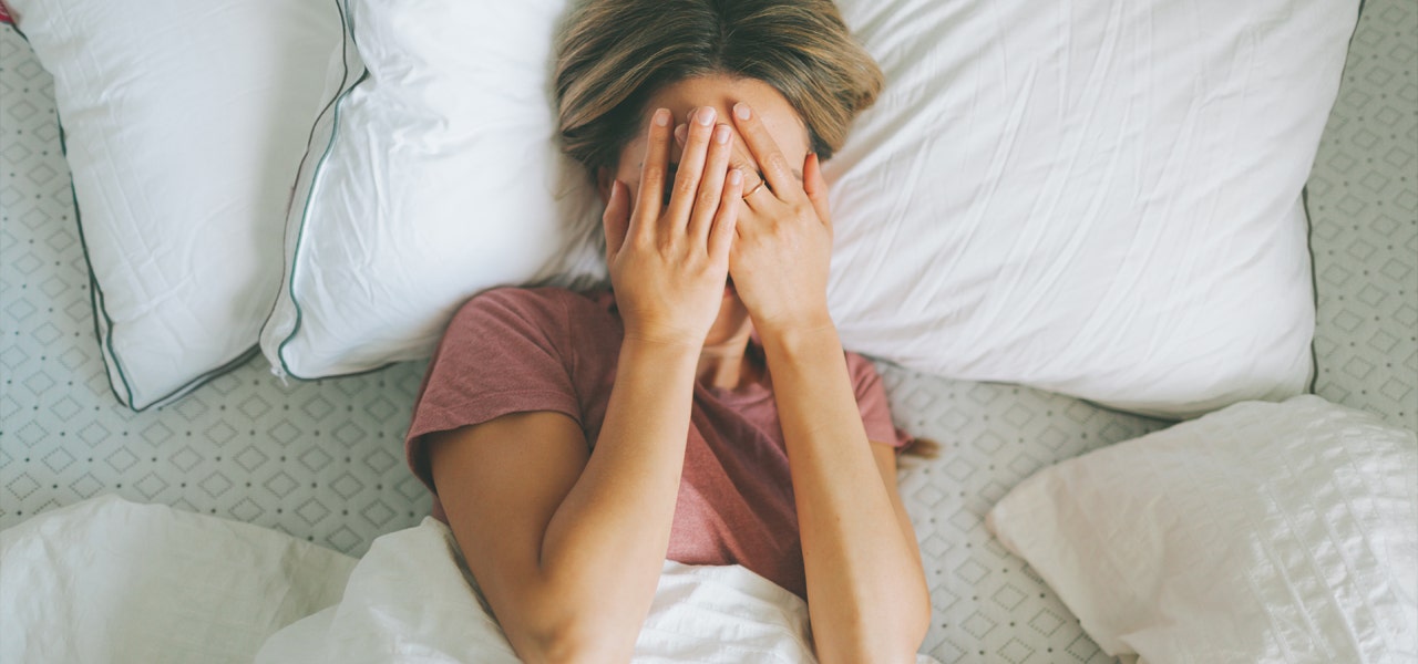 Woman lying awake in bed and covering her face with her hands 