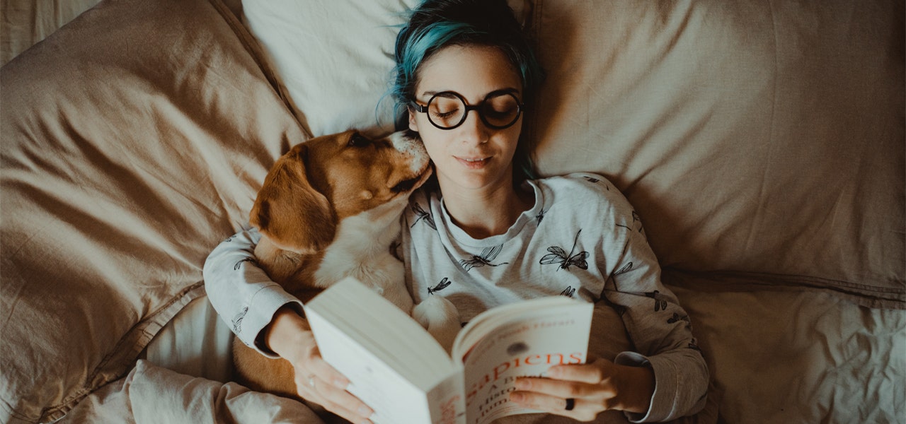 Woman reading a book in bed and snuggling her dog 