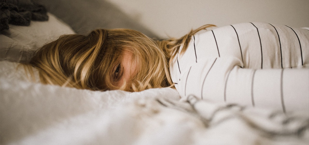 Woman lying facedown on her bed and looking very sleepy