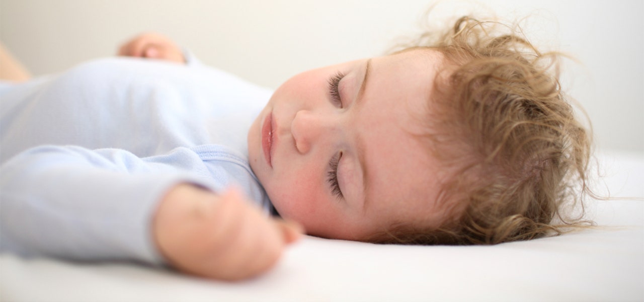 Baby with curly hair sleeping on a firm crib mattress