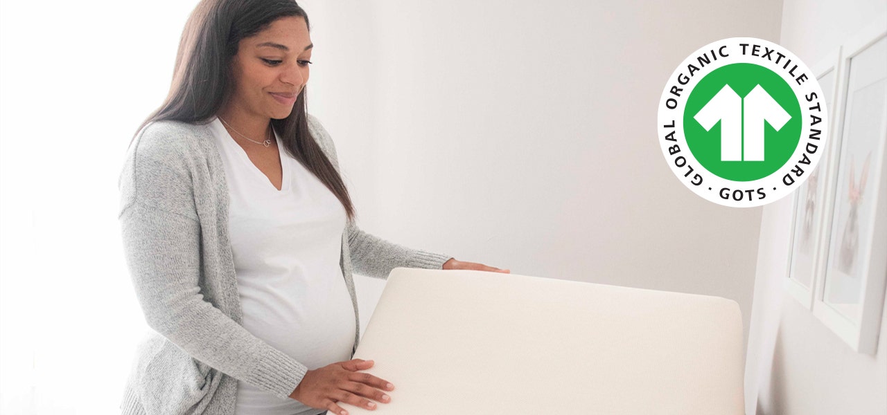 Pregnant mother looking at her GOTS certified Naturepedic crib mattress, GOTS logo