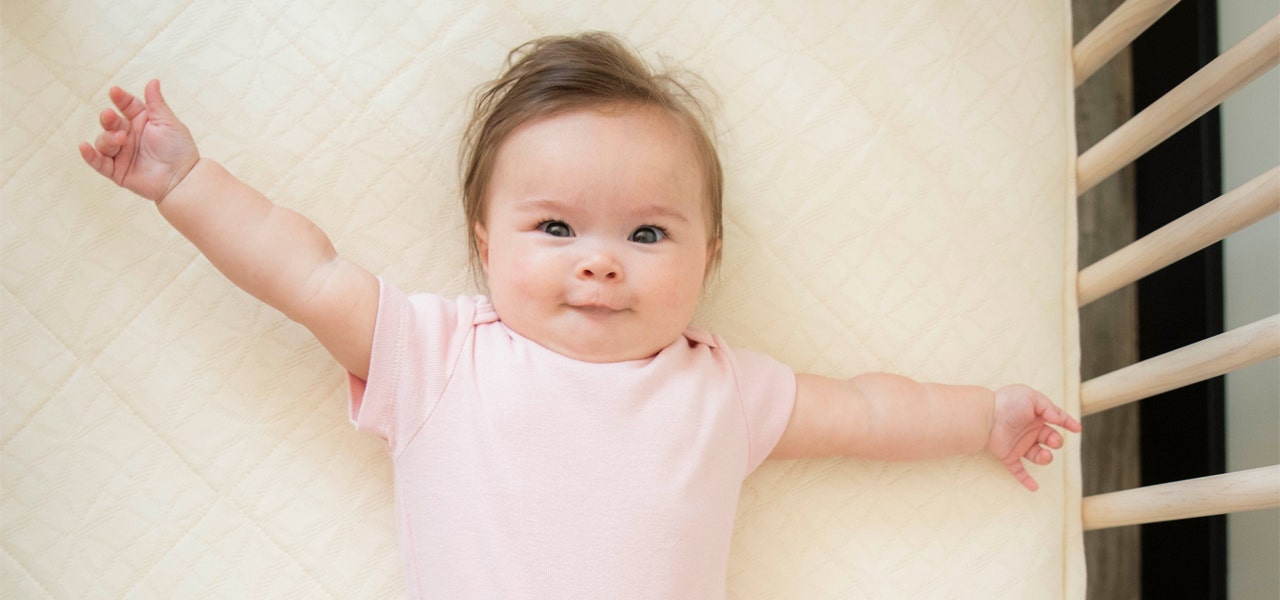 Smiling, wide-awake baby on a Naturepedic breathable, waterproof mattress