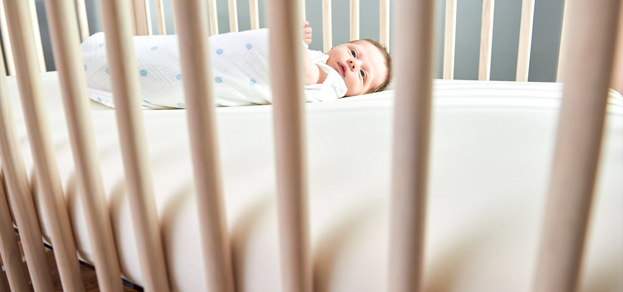 Swaddled newborn baby lying on their back in a crib