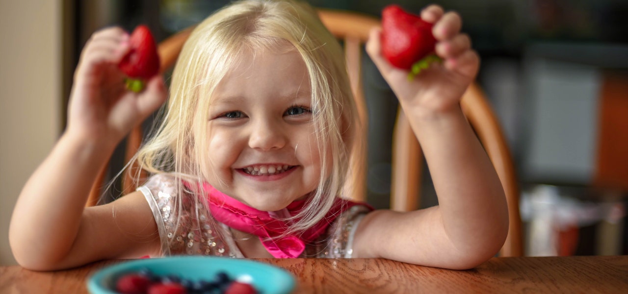 Young girl holding up strawberries and smiling 