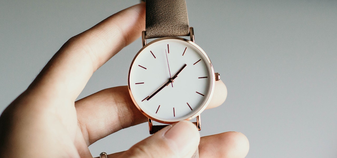 Person's hand holding a watch, preparing for DST