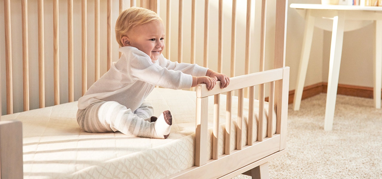 Toddler sitting up and smiling on a 2-stage mattress