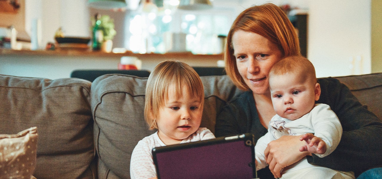 Mom sitting on a couch with her baby and toddler, looking at a laptop