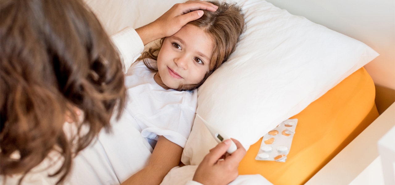 Mother tucking her daughter into bed and taking her temperature