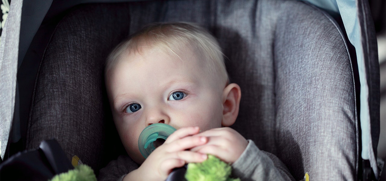 Baby wide awake in their carseat with a green pacifier in their mouth