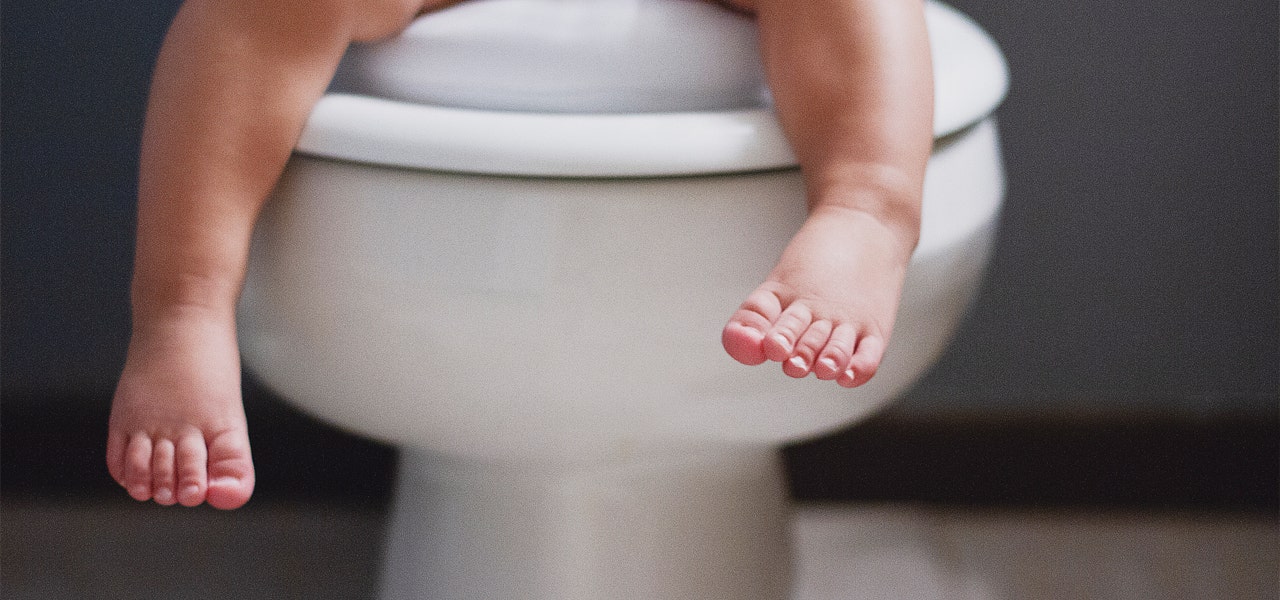 Toddler's bare feet dangling over the edge of the toilet seat