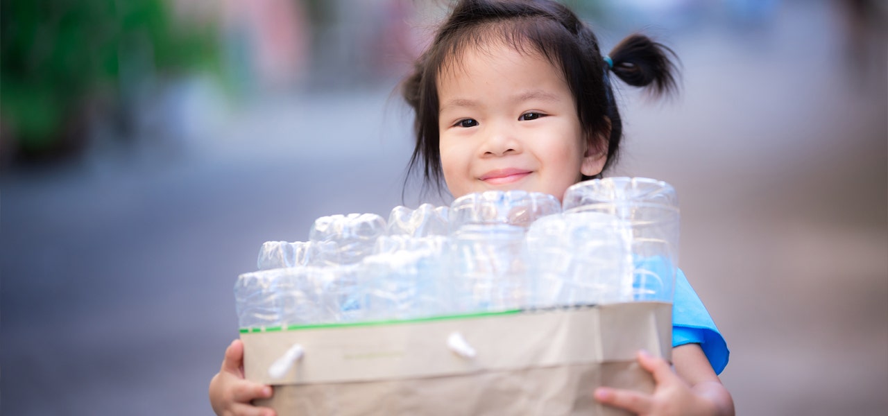 Preschooler carrying a paper bag full of recycling