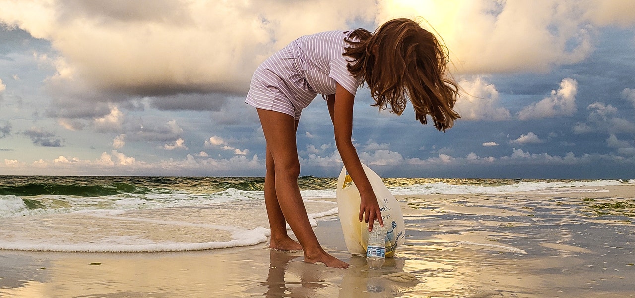 Elementary school-aged girl picking up trash on the beach at sunset