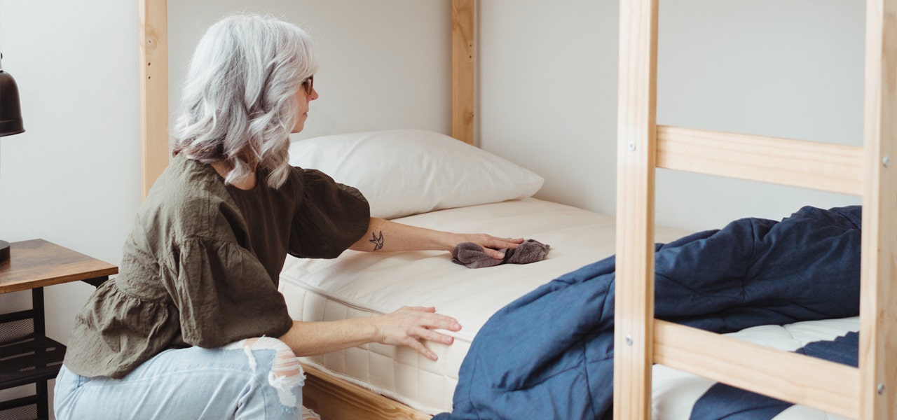 Woman kneeling next to kids bed and wiping clean the waterproof mattress