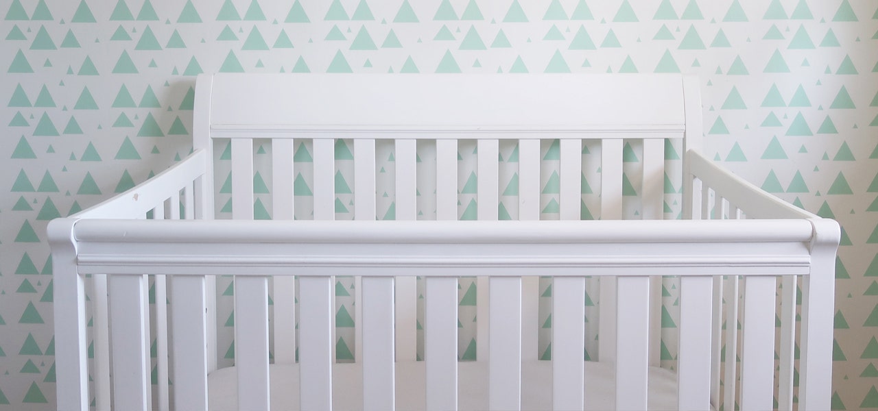 White crib against a wall with a green triangle pattern 