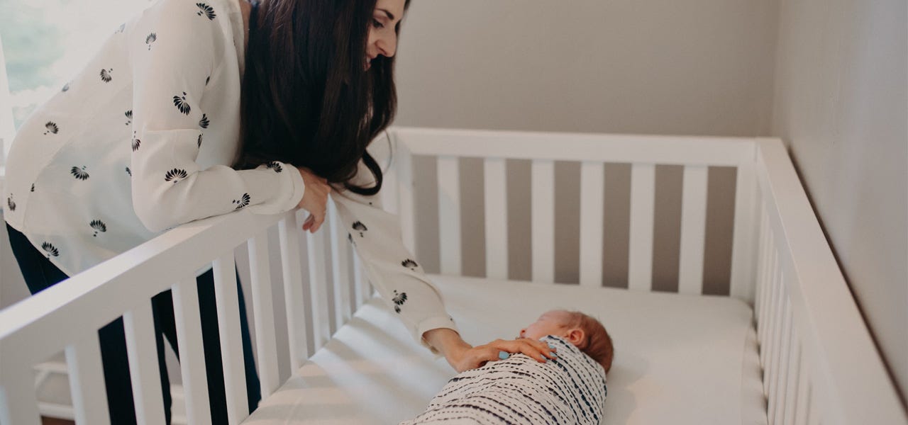 Mother leaning over crib to settle baby, crib in the corner