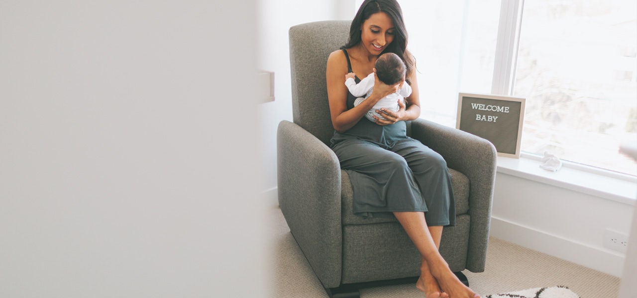 Mother sitting in a gliding chair and smiling at her baby