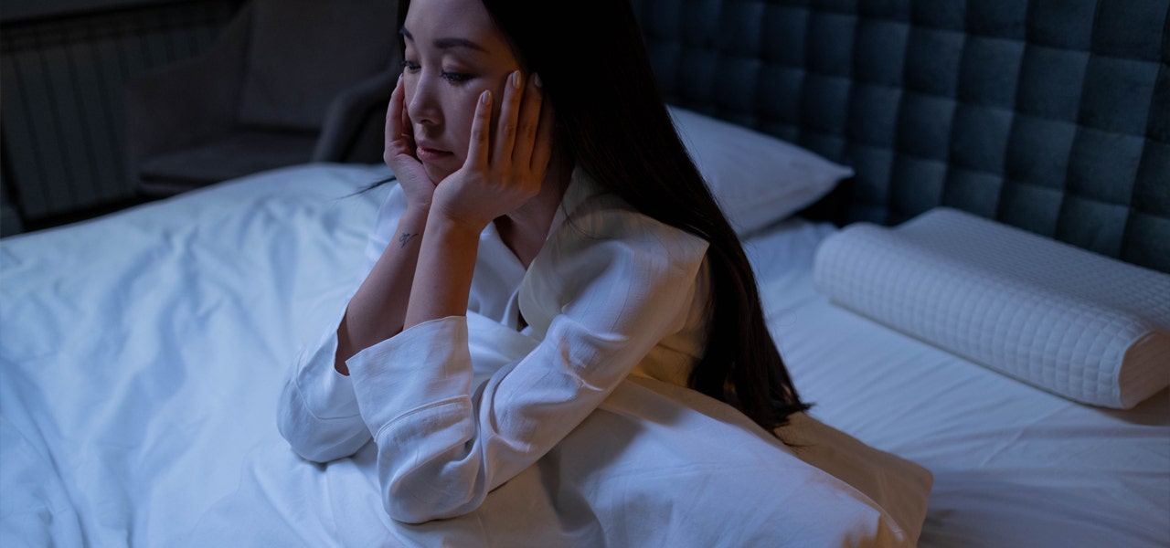 Woman sitting up in bed at night, unable to sleep