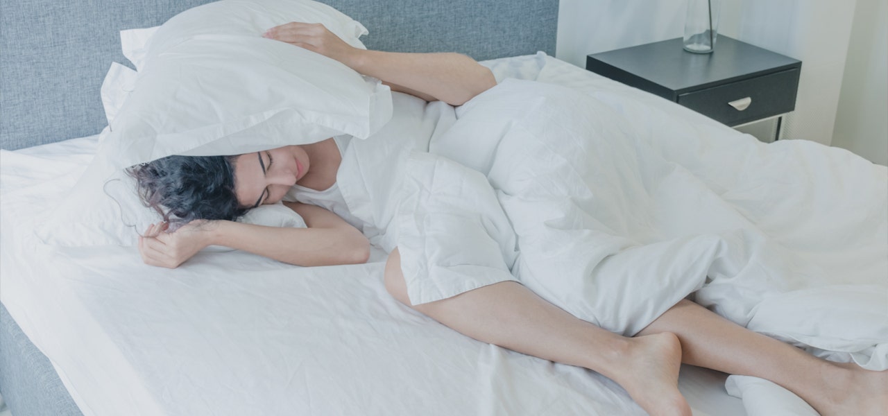 Woman in bed with pillow over her head to block the sunlight