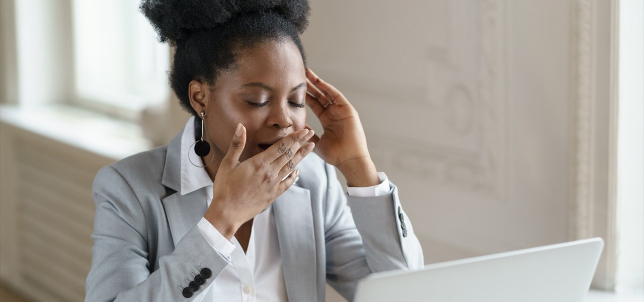 Woman yawning at her computer in an office setting 