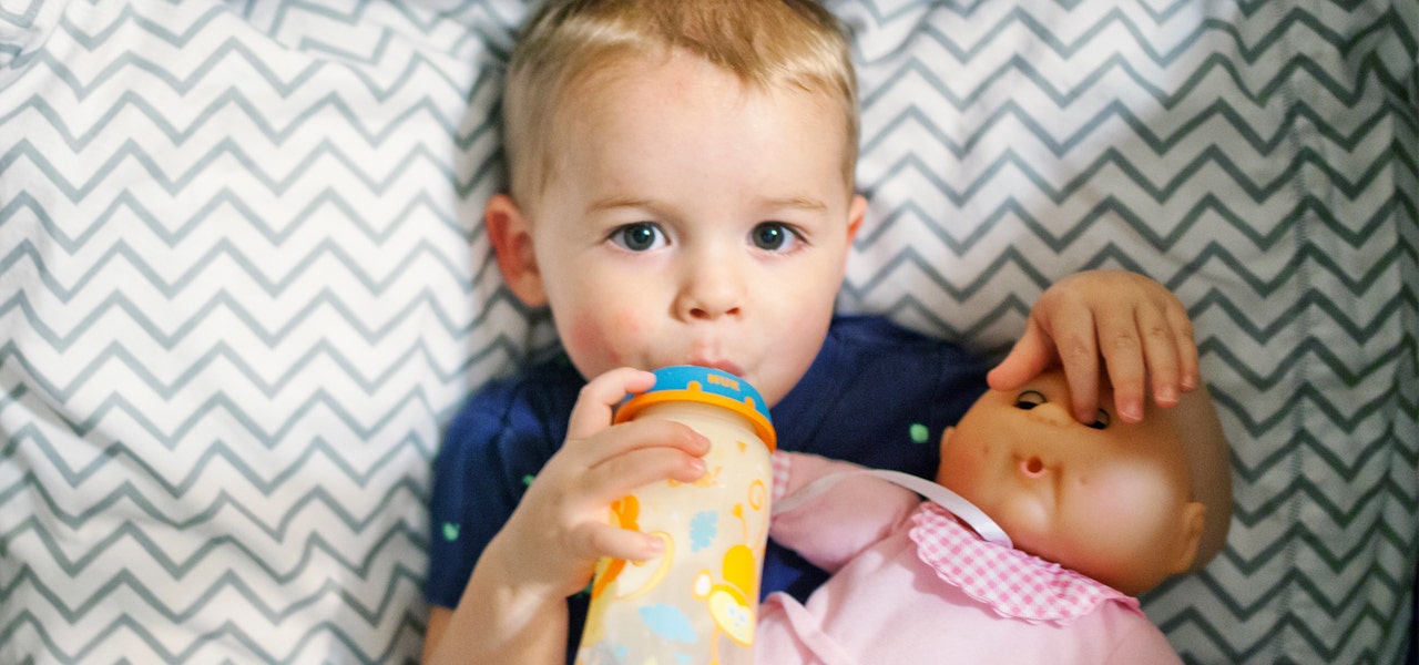Small boy drinking a bottle and holding a doll