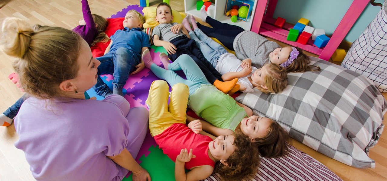 Preschool teacher sitting on the floor with a group of kids during naptime 