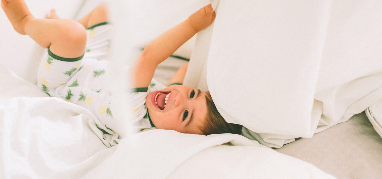 Small child rolling around playfully in a big kid bed