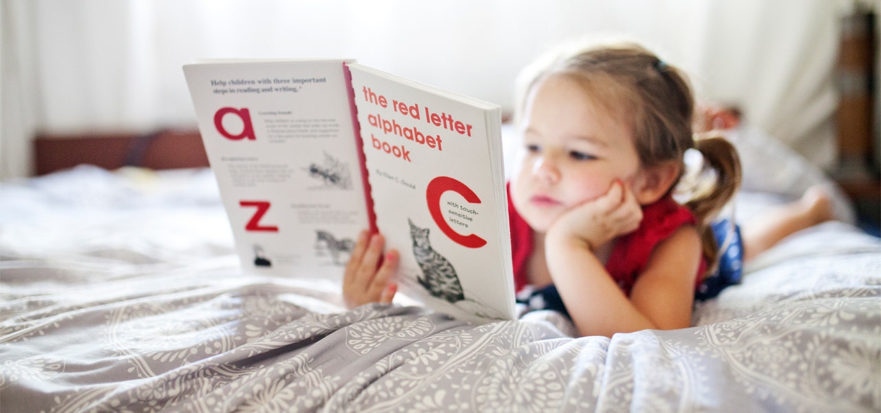 Toddler quietly looking at a book in bed instead of napping