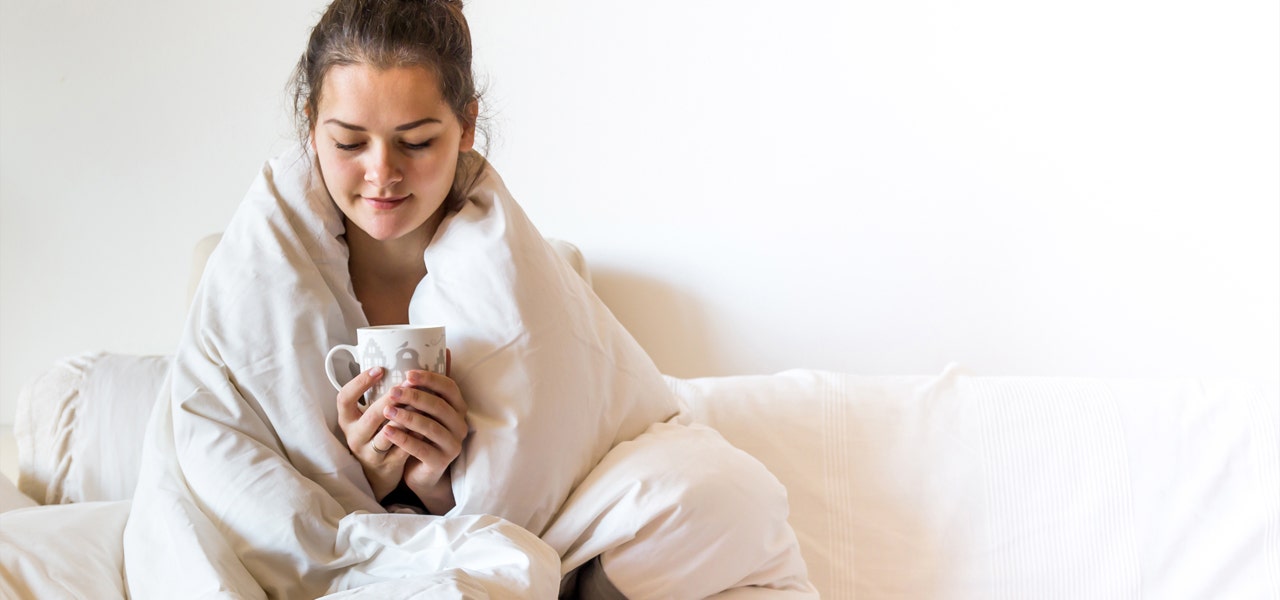 Well rested woman sitting up and drinking coffee in bed