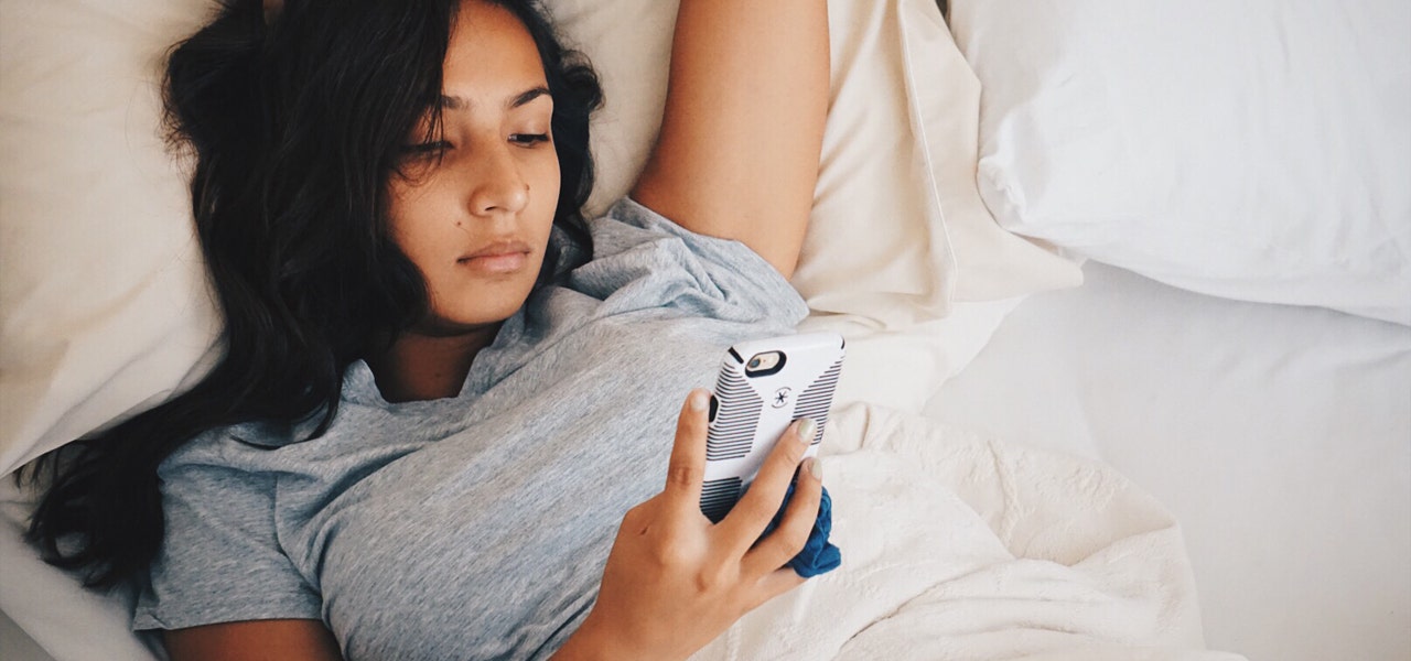 Young woman scrolling through her phone in bed