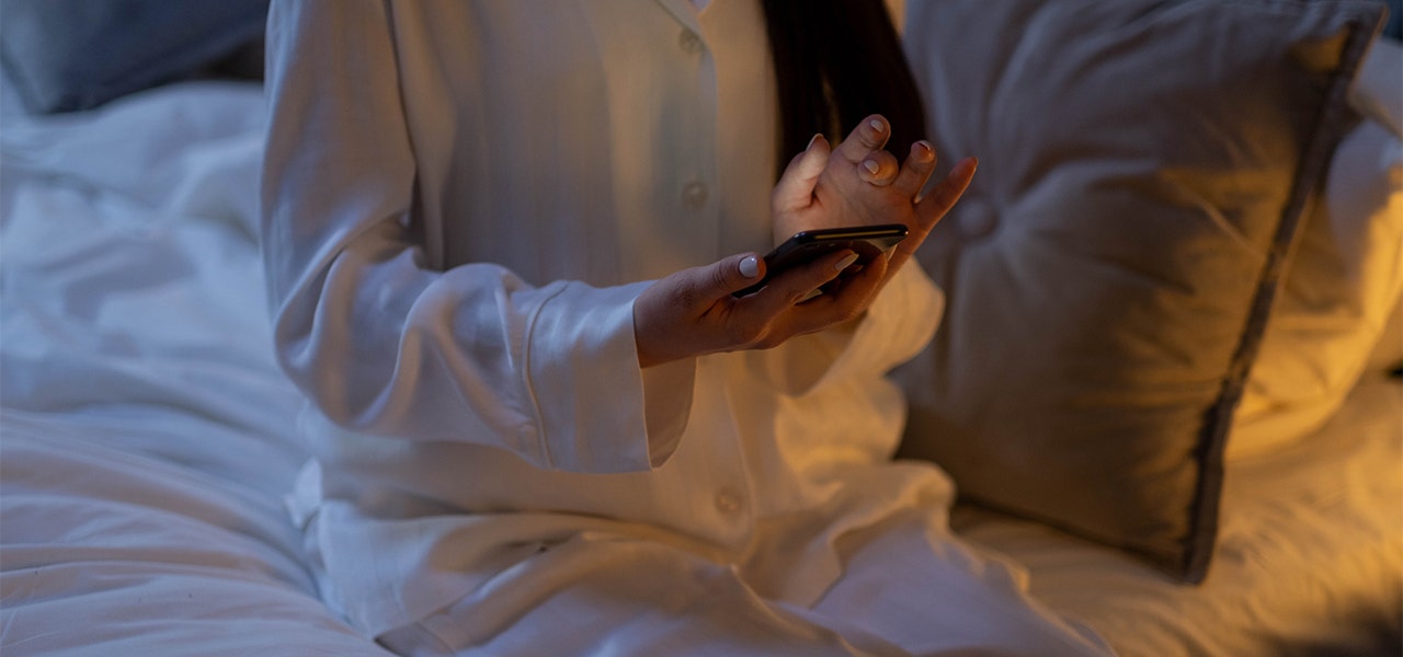 Woman sitting up in bed and scrolling through her phone